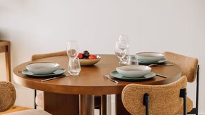 Una mesa redonda de comedor con cuatro platos, dos copas de vino y un cuenco de fruta.