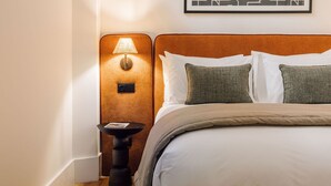 Habitación de hotel con una cama, dos almohadas, una mesita de noche, una lámpara y un cuadro en la pared.