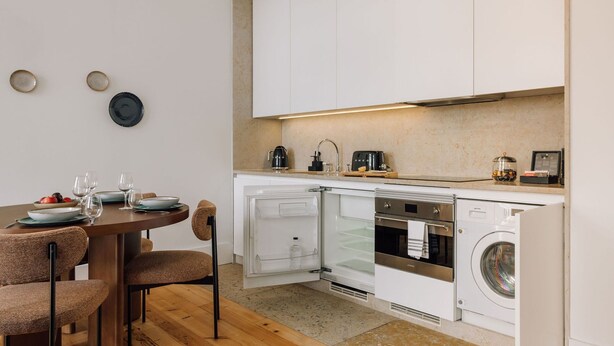 Una cocina compacta con horno integrado, microondas y lavavajillas. Hay una mesa de comedor con sillas y un refrigerador pequeño.