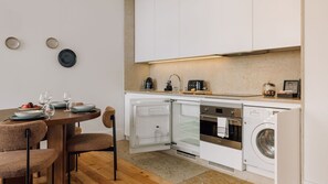 Una cocina compacta con horno integrado, microondas y lavavajillas. Hay una mesa de comedor con sillas y un refrigerador pequeño.