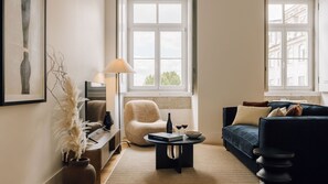 A living room with a sofa, a chair, a coffee table, and a lamp. There is a window with a view of buildings outside. - Ando Living - Corpo Santo House - 201 (Lisbon)