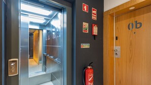 Interno di un ascensore con un estintore fissato alla parete e una porta in legno con la lettera 'b'.