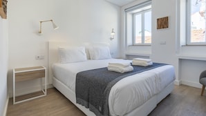 Una camera d'albergo moderna con un letto grande, un comodino, una finestra con vista e una lampada a parete.