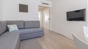 Egy modern nappali, szürke színű kanapéval, a falra szerelt, síkképernyős televízióval és fa padlóval.