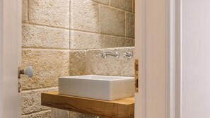 Ein Badezimmer mit einem weißen Waschbecken auf einem Holzboden, Steinwänden und einer Tür mit einem runden Griff.