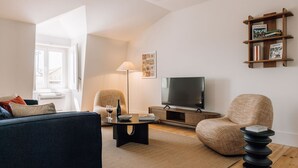 Un salon comprenant un canapé, un fauteuil, une table basse, un téléviseur et une bibliothèque.
