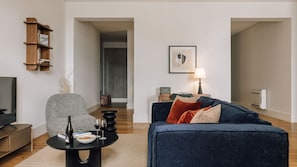 A modern living room with a sofa, a coffee table, a bookshelf, a TV, and a lamp. - Ando Living - Corpo Santo House - 102 (Lisbon)