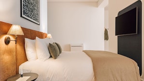 Une chambre d’hôtel comprenant un lit, une table de chevet, une lampe, un téléviseur fixé au mur et un tableau encadré.