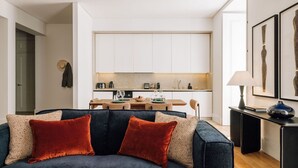 Un salon moderne avec un canapé bleu foncé, des coussins rouges et un coin repas comprenant une table et des chaises en bois.