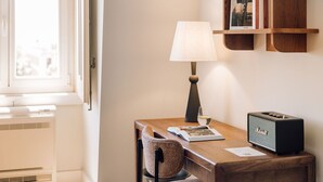 A hotel room with a wooden desk, a lamp, a chair, a radio, and a window with blinds. - Ando Living - Corpo Santo House - 501 (Lisbon)