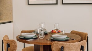 Une table de salle à manger ronde, accompagnée de quatre chaises, de verres transparents et d’un saladier rempli de fruits.
