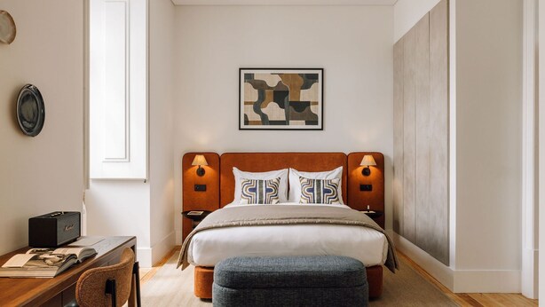 Une chambre moderne avec une tête de lit en bois, deux lampes de chevet, une décoration murale à motifs et une petite table de chevet avec une lampe.