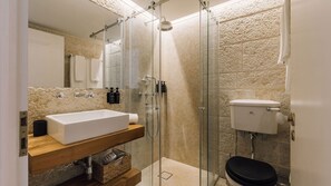 Un baño moderno con ducha de vidrio, tocador de madera con lavamanos blanco y un inodoro.