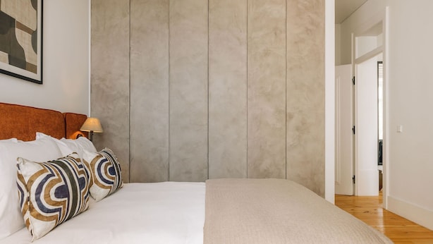 A bedroom with a bed, pillows, a headboard, a lamp, and a door leading to another room. - Ando Living - Corpo Santo House - 101 (Lisbon)