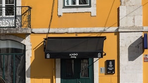 A building with a yellow facade, a black awning with "ANDO Living" signage, a green door, and a small plaque indicating "CORPO SANTO HOUSE". - Ando Living - Corpo Santo House - 101 (Lisbon)