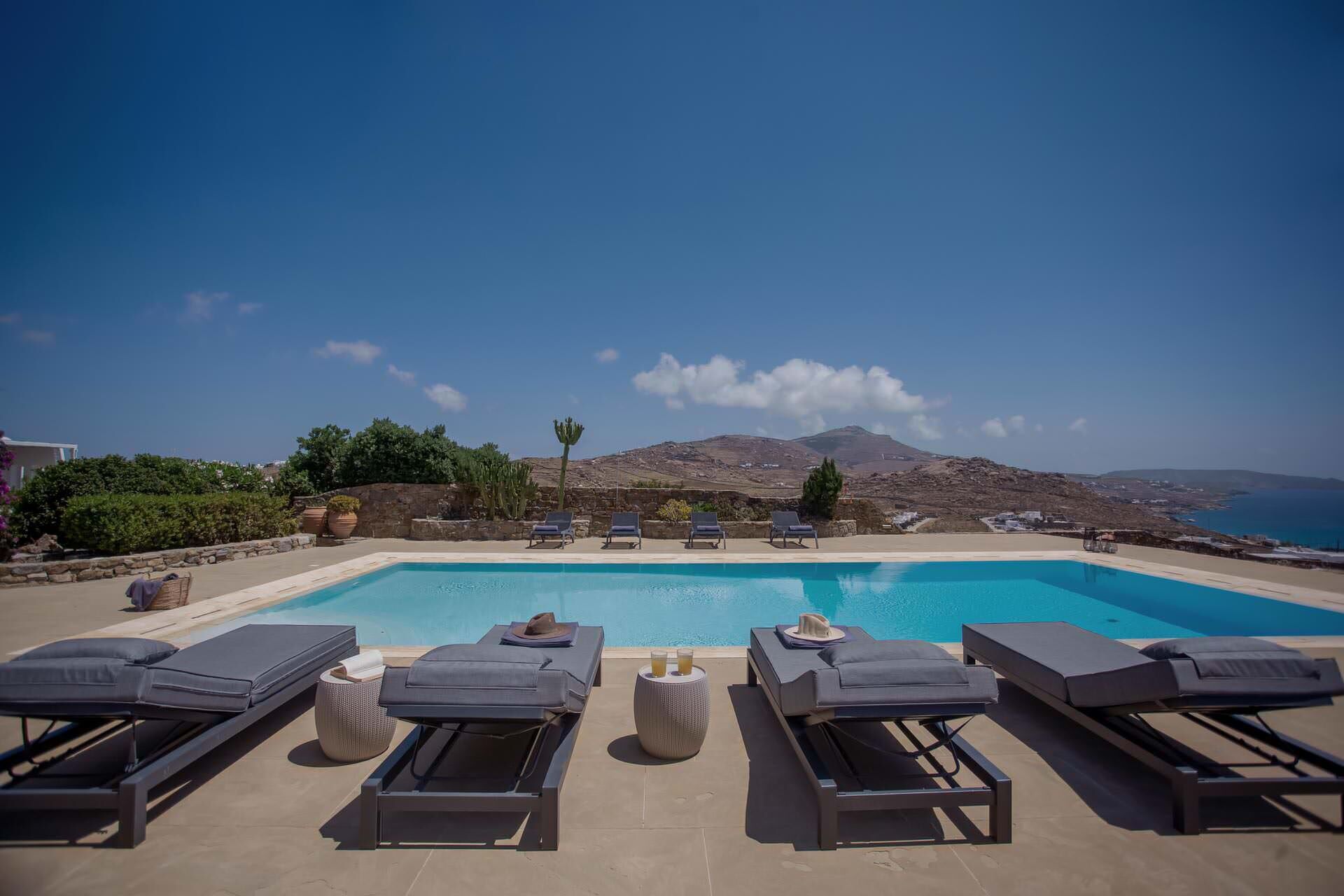 A poolside area with lounge chairs and a view of the sea and mountains.