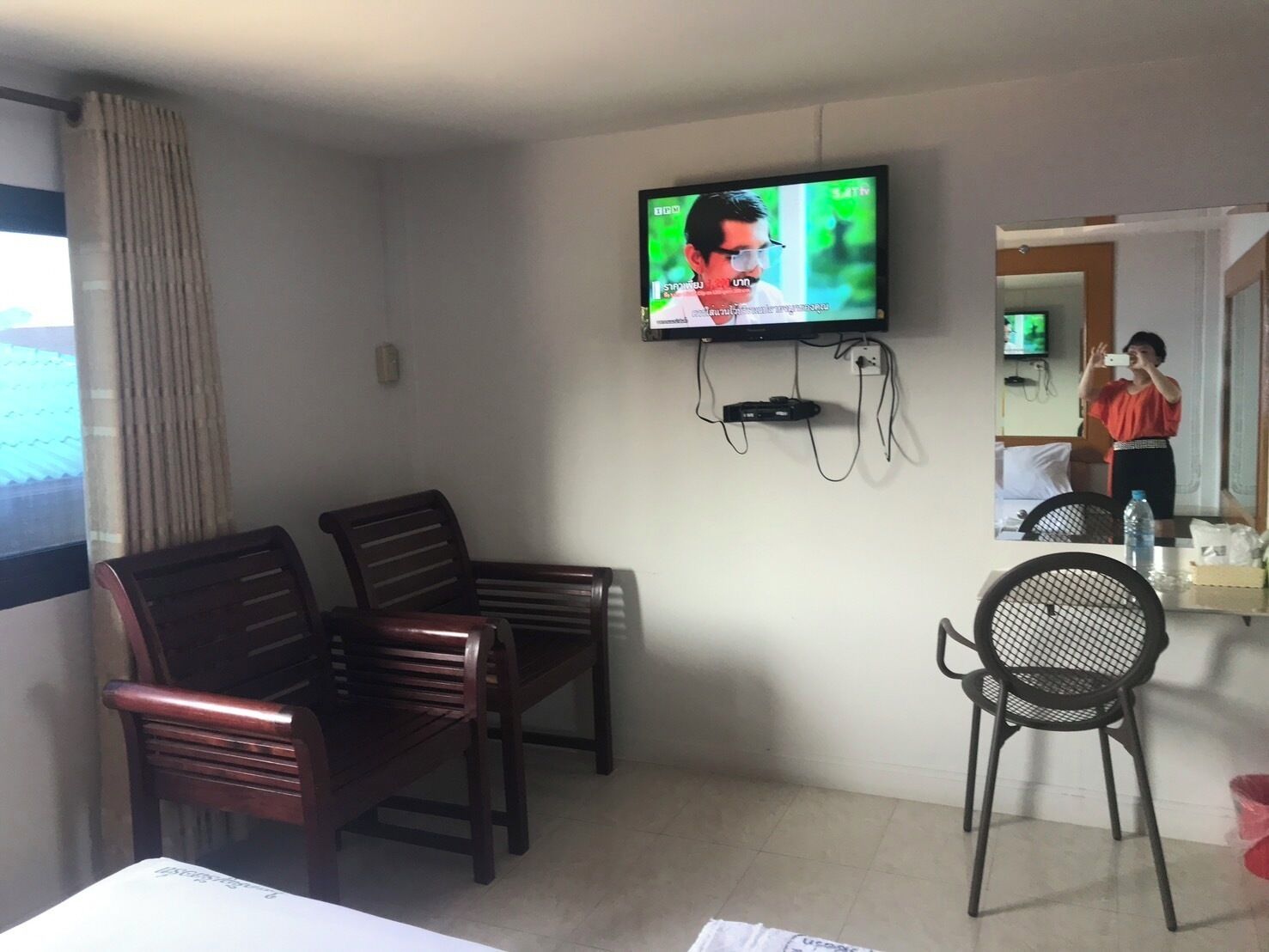 Een hotelkamer met een aan de muur bevestigde televisie, een houten stoel, een eettafelstoel en een bed.