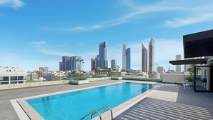 Une piscine sur le toit offrant une vue panoramique sur la ville, un espace salon couvert et une façade d’immeuble moderne.