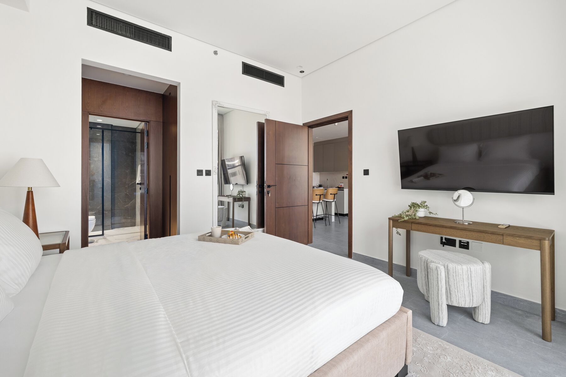Quarto de hotel moderno com uma cama grande, uma mesa de trabalho, uma televisão e um banheiro visível por uma porta aberta.