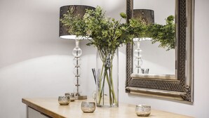 A wooden dresser with a mirror, a vase with green plants, and two small bowls. - Queen's Gate Gardens Flat (London)