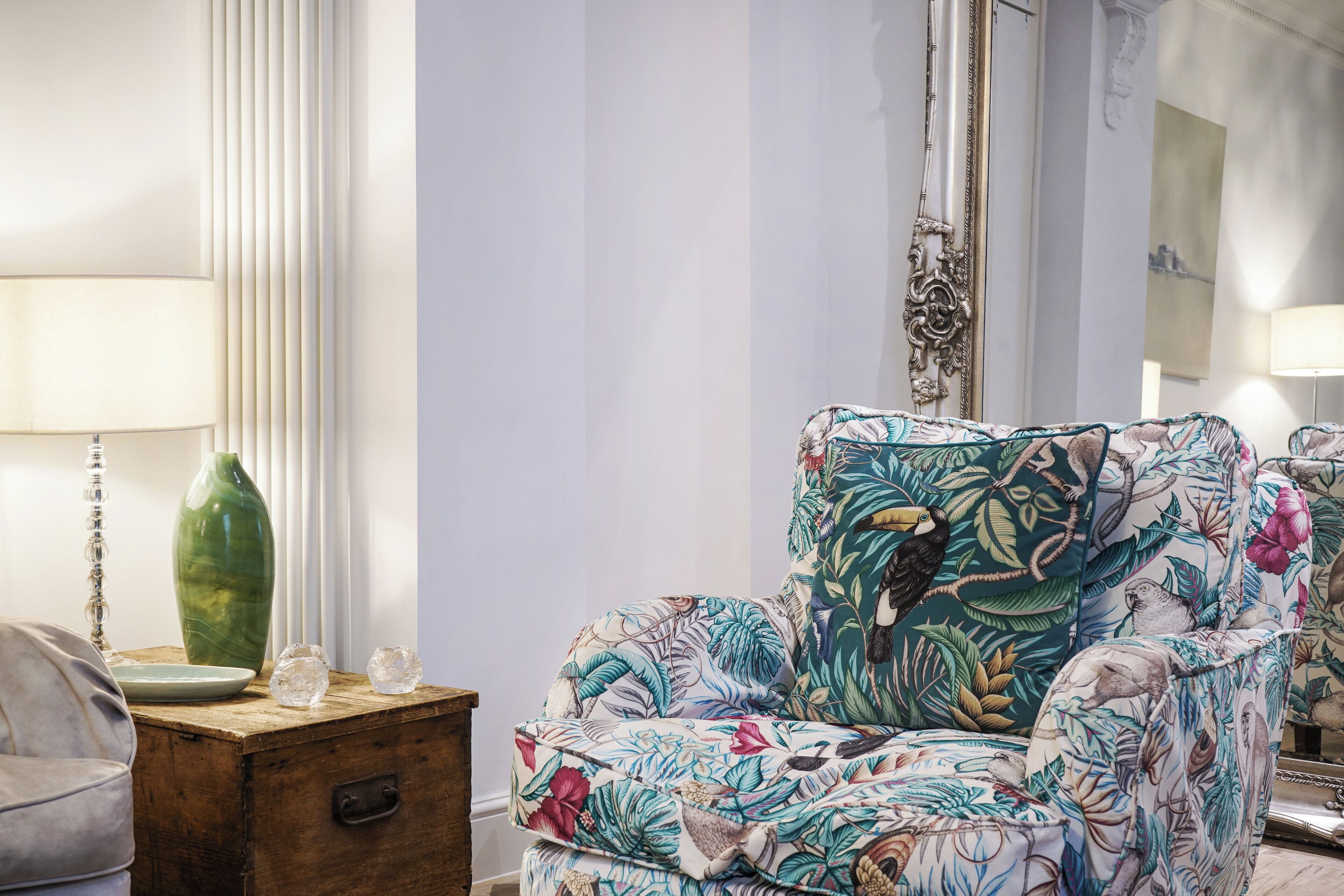 Une pièce comprenant un fauteuil à motifs floraux, une table d’appoint en bois ornée d’objets décoratifs et une lampe.