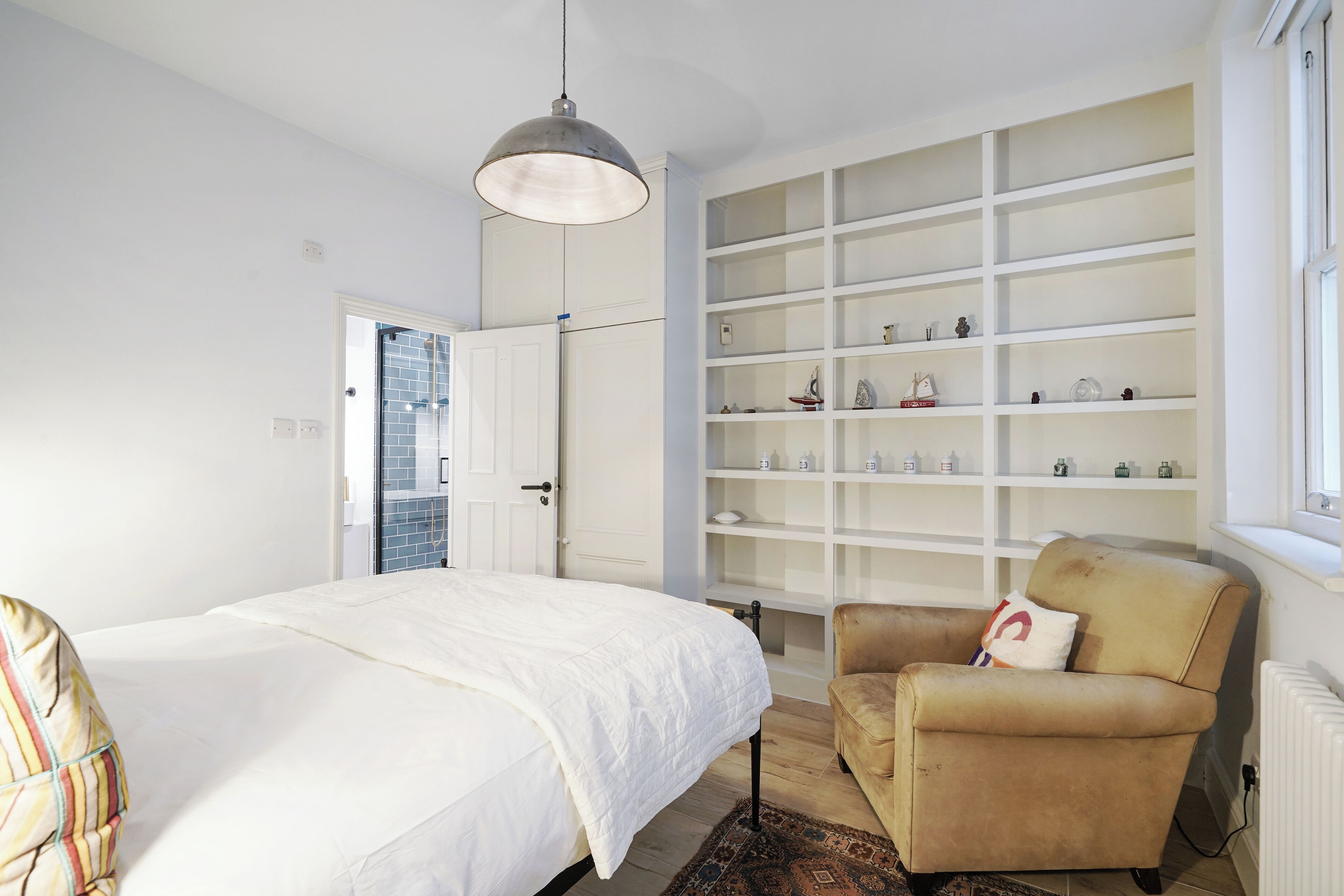 Een slaapkamer met een bed, een stoel, een wandplank en een raam.
