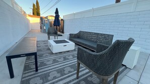 En patio med en hvid murstensvæg, et mønstret tæppe, et hvidt sofabord, en fletsofa og en stol.