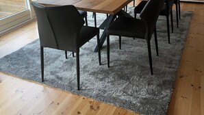Ein Essbereich mit Holztisch, schwarzen Stühlen, großen Fenstern und einem grauen Teppich.