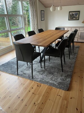 A dining area with a wooden table and black chairs, large windows, and a grey carpet. - Holiday home near beach nature and activities (Væggerløse)