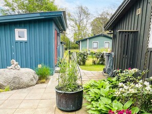 Un quartier résidentiel avec une maison bleue, un abri de jardin noir et un jardin agrémenté de plantes et de fleurs en pot.