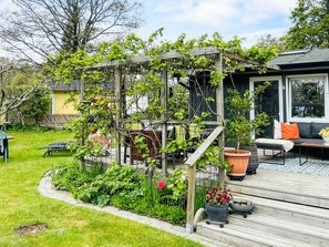 Une terrasse en bois surmontée d’une pergola, entourée d’une végétation luxuriante et de plantes en pot.