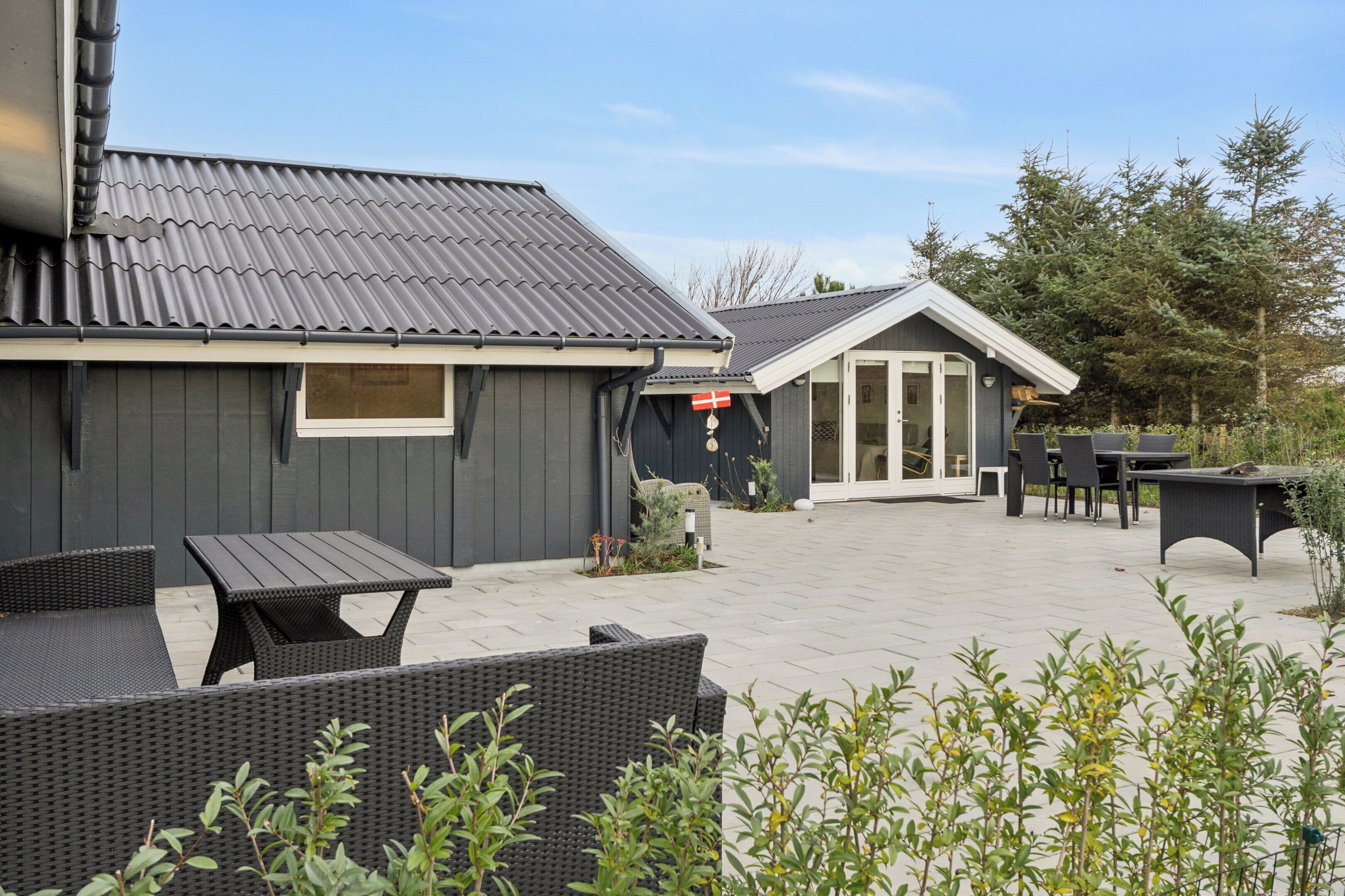En terrasse med udendørs møbler, en bygning med mørk facade, og et flag.