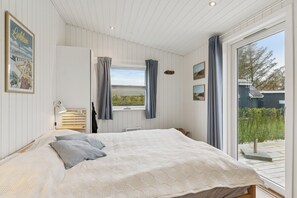 A bedroom with a large bed, a window with curtains, a headboard, and a view of the outdoors. - Holiday Paradise near Grønhøj Beach (Løkken)