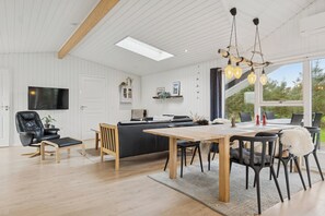 A modern interior with a dining area, a sofa, a TV, and a large window. - Holiday Paradise near Grønhøj Beach (Løkken)