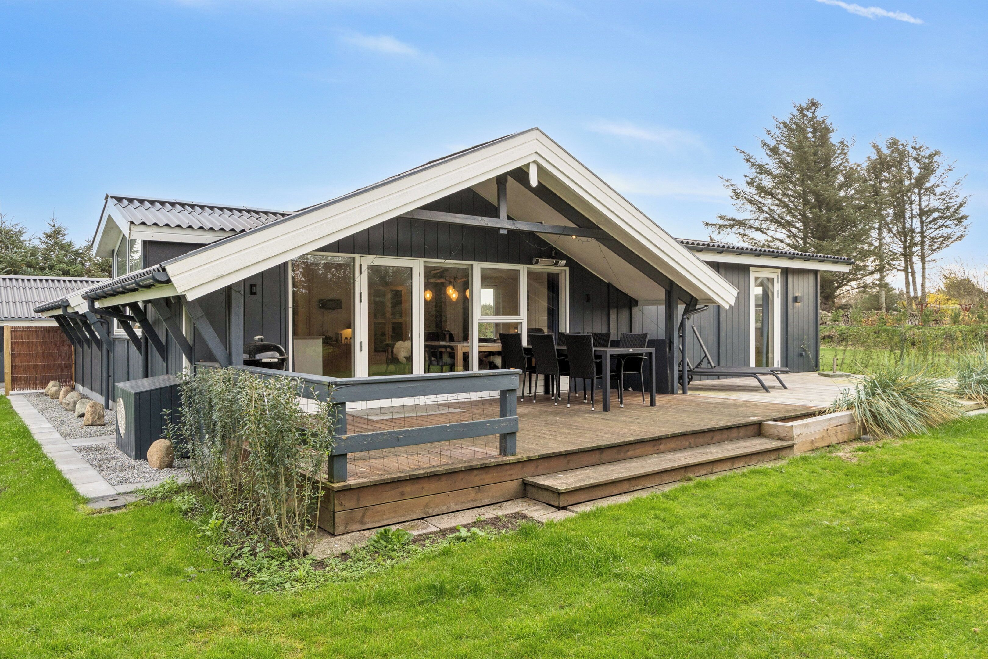 Een modern huis met een terras, grote ramen en een eethoek.