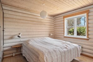 A log cabin bedroom with a bed, a window, a lamp, and a ceiling light. - Lovely log house on Møn (Stege)