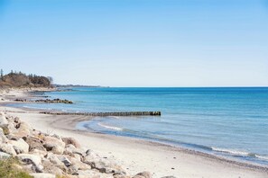 Een strand met een rotsachtige kustlijn, een houten golfbreker en een helderblauwe lucht.