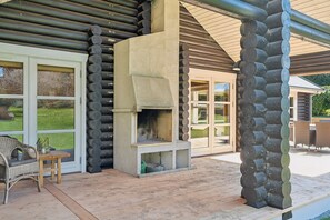 A log cabin with a stone fireplace, a covered patio, and a wicker chair. - Lovely log house on Møn (Stege)