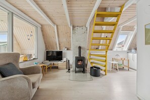 Ett rum i loftstil med ett träpanelat tak, en tv, en öppen spis, en gul spiralformad trappa och ett fönster med utsikt över en terrass.
