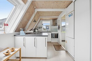 A modern kitchen with white cabinets, a wooden ceiling, and a view through a window. - Lovely holiday home with sea view (Otterup)