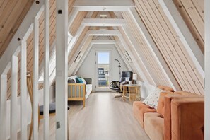 Ett rum i loftstil med ett sluttande tak, synliga träbjälkar, en soffa, en fåtölj och ett litet bord.