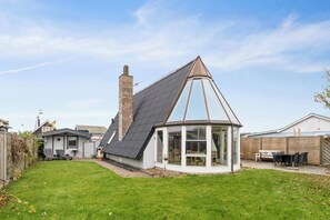 Ein Haus mit einem Giebeldach, einem Wintergarten und einem eingezäunten Garten.