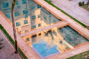 Una piscina con un motivo geometrico in piastrelle, circondata da un percorso pedonale lastricato e da una palma.