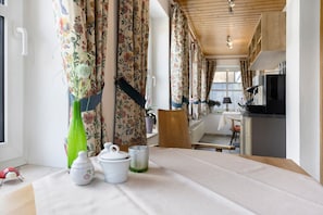 A room with a table set for tea, a chair, a wooden cabinet, and a window with curtains. - Laura’s Country Guesthouse – Family Room (Double Room with Adjoining Children’s Room) (Medebach)