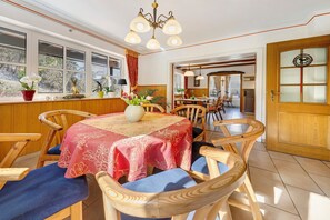A dining area with a round table, wooden chairs, a chandelier, and a view through a window. - Laura’s Country Guesthouse – Family Room (Double Room with Adjoining Children’s Room) (Medebach)