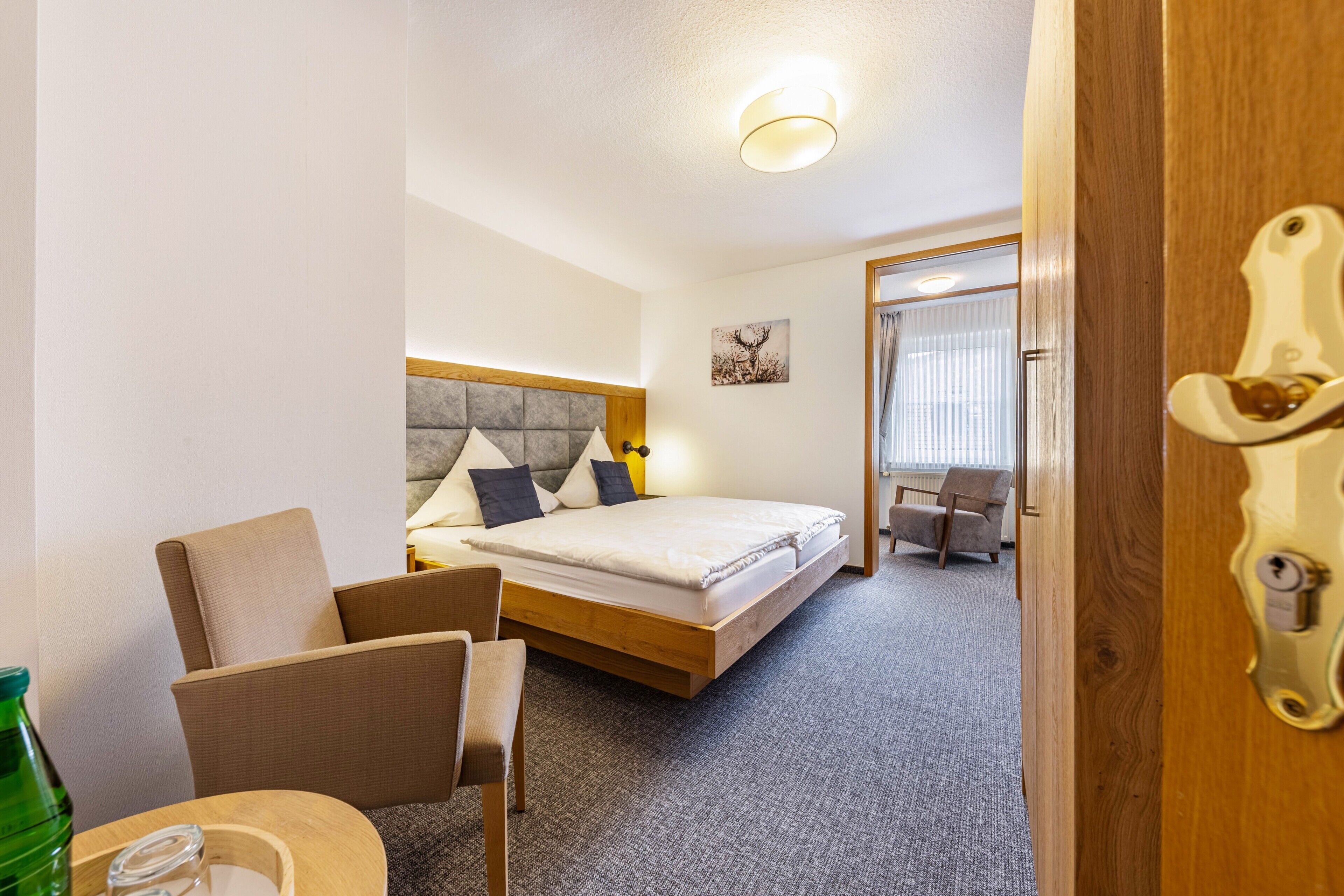 A hotel room with a bed, a chair, a table, and a door.
