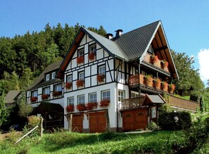 A traditional half-timbered house with multiple windows, a balcony with flower boxes, and a garage. - Laura’s Country Guesthouse – Family Room (Double Room with Adjoining Children’s Room) (Medebach)