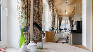 Ein Zimmer mit Tisch, der für Tee gedeckt ist, einem Stuhl, einem Holzschrank und einem Fenster mit Vorhängen.