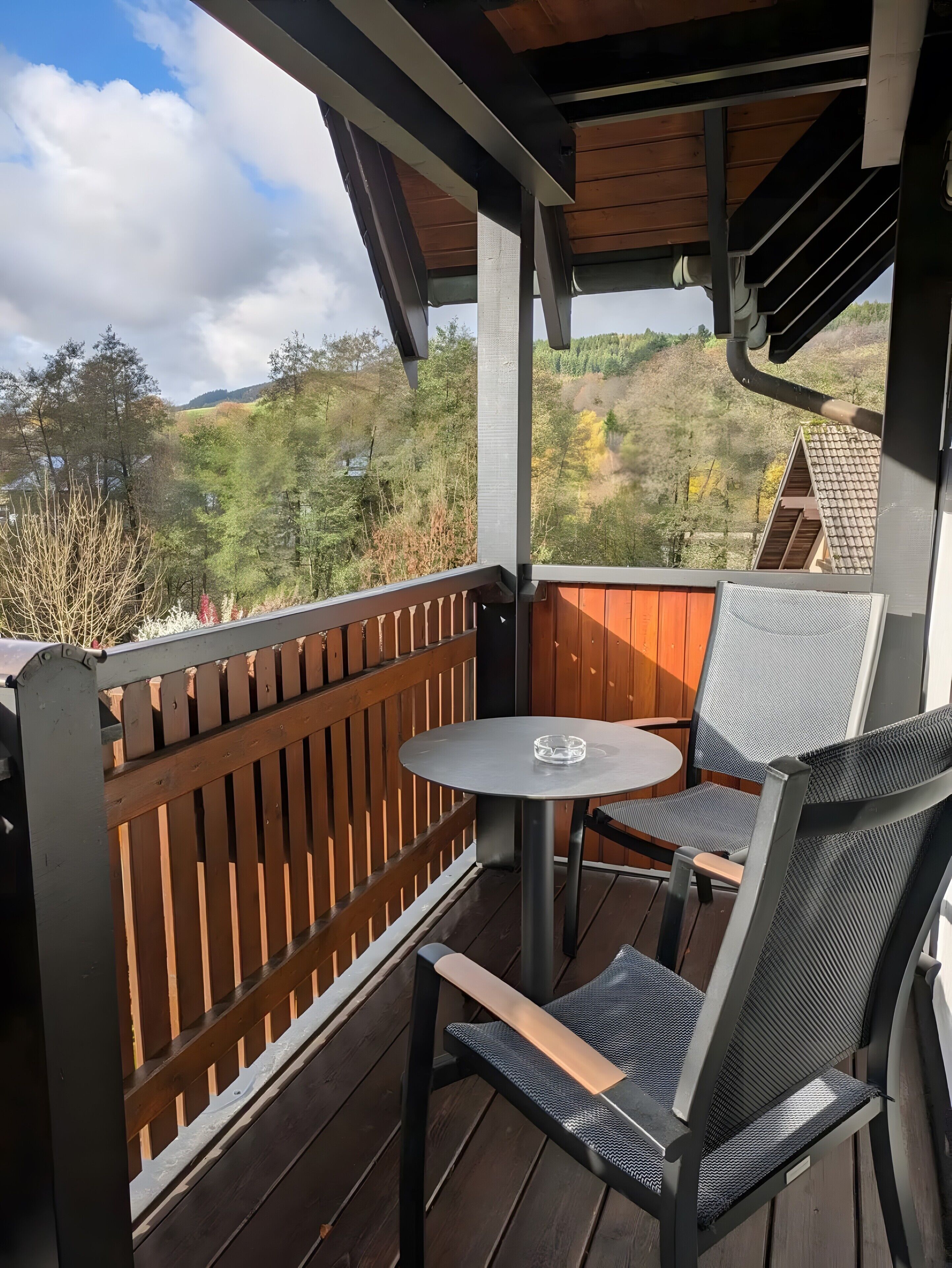 Een overdekt terras met een tafel en stoelen, met uitzicht op een glooiend landschap.