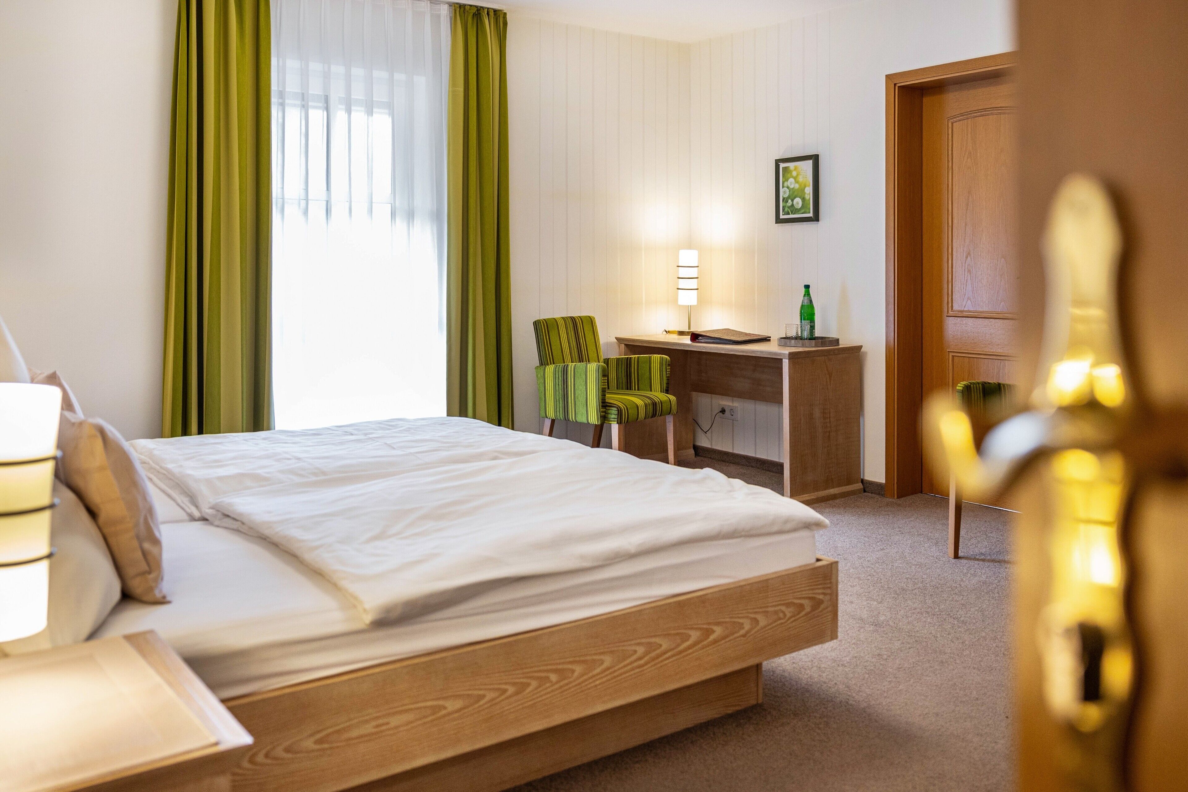 Een hotelkamer met een bed, bureau, stoel, lamp en een deur.